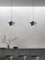Two small black-and-walnut Clérachic pendants hang above a grey concrete-look counter with three dark stools.
