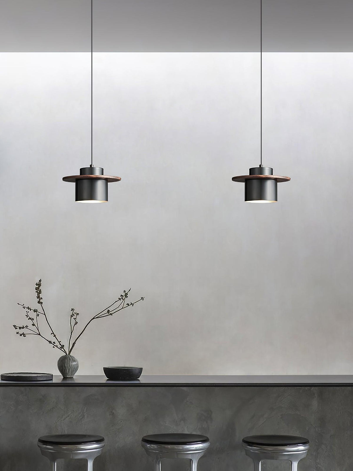 Two small black-and-walnut Clérachic pendants hang above a grey concrete-look counter with three dark stools.