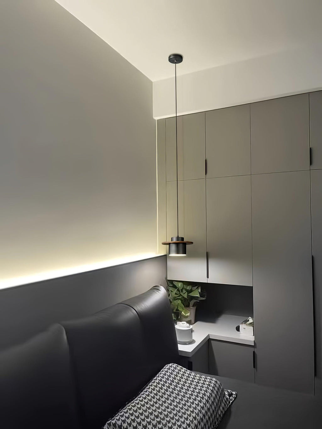 A Clérachic pendant with a dark shade hangs above a bed in a grey room with wall cabinets and a strip of warm light.