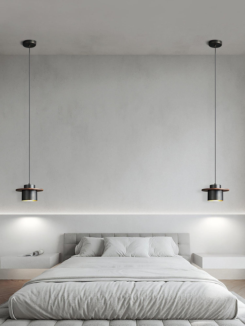 A pair of black-and-walnut Clérachic pendants hang either side of a grey bed against a pale plaster wall.