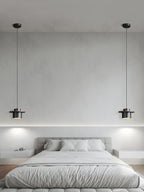 A pair of black-and-walnut Clérachic pendants hang either side of a grey bed against a pale plaster wall.