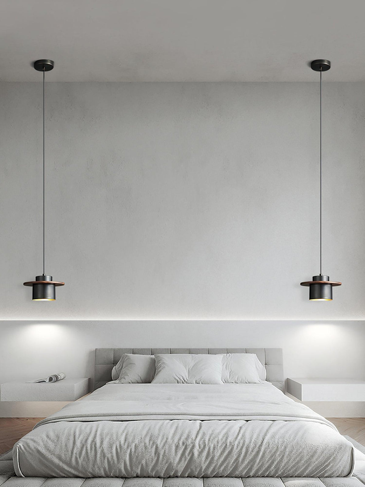 A pair of black-and-walnut Clérachic pendants hang either side of a grey bed against a pale plaster wall.