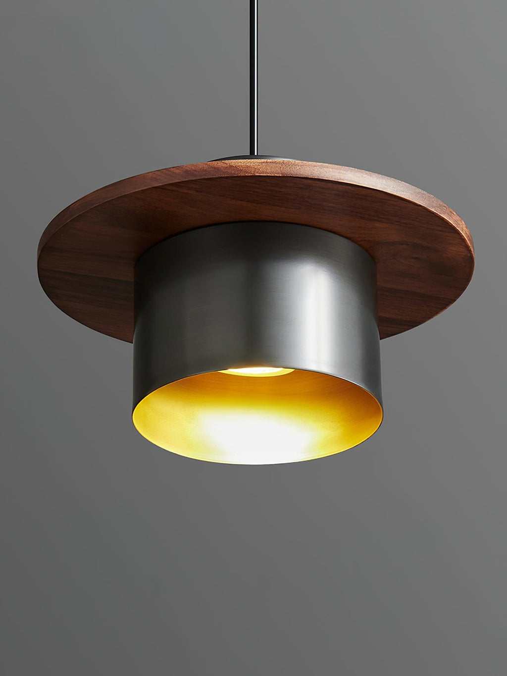 Low view into a black-and-walnut Clérachic pendant, showing the brass-coloured interior and a lit bulb.