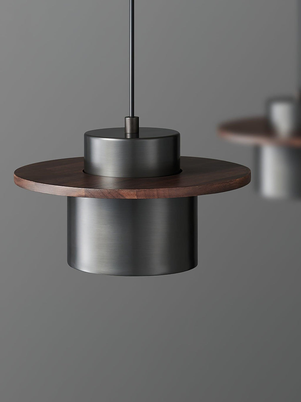 Black cylinder shade under a round walnut brim on this Clérachic pendant, with a second pendant softly blurred behind.