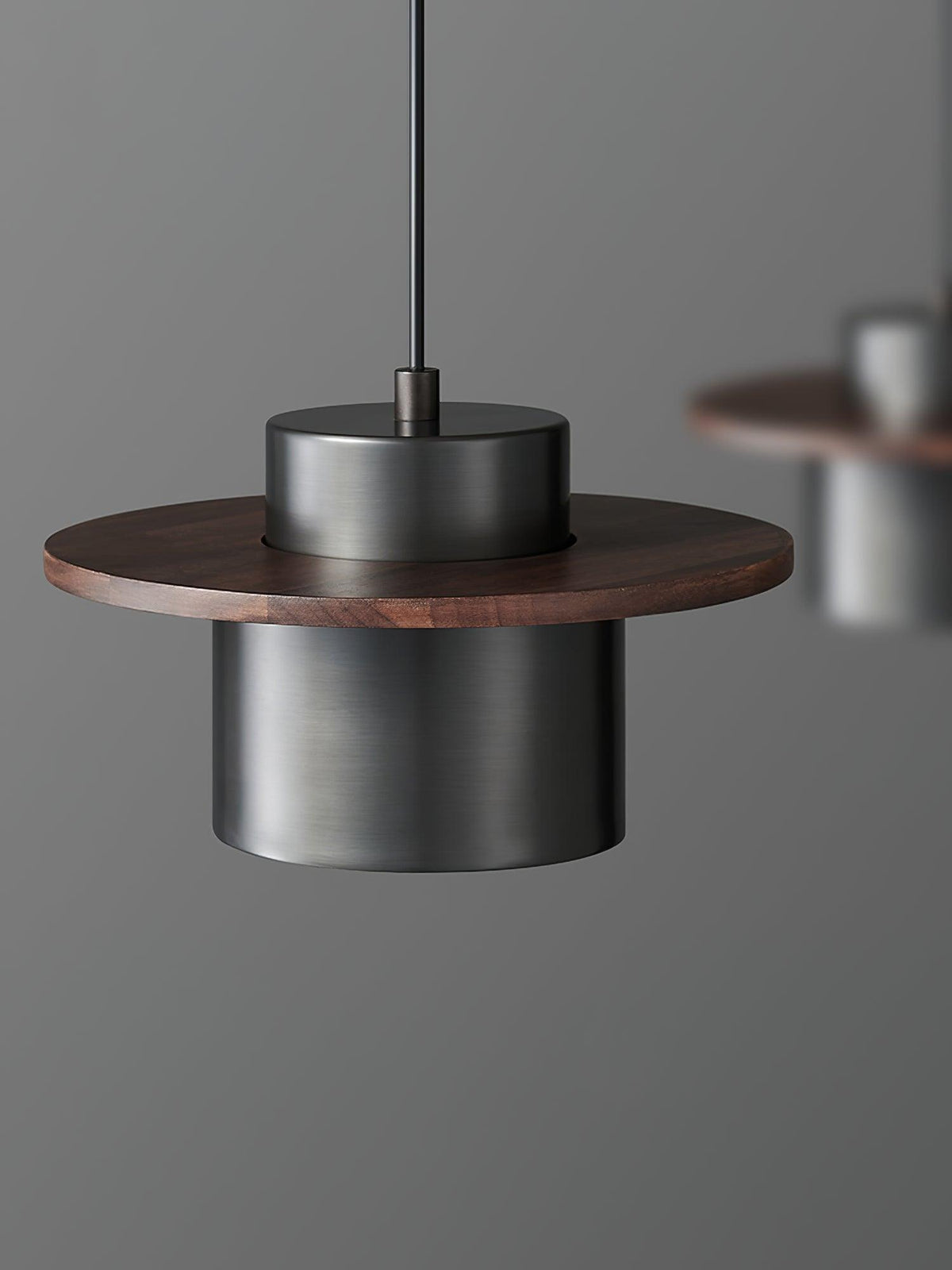 Black cylinder shade under a round walnut brim on this Clérachic pendant, with a second pendant softly blurred behind.