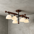 Five frosted glass shades hang below walnut-finished wood bars on this Clérachic semi flush light, against grey plaster.