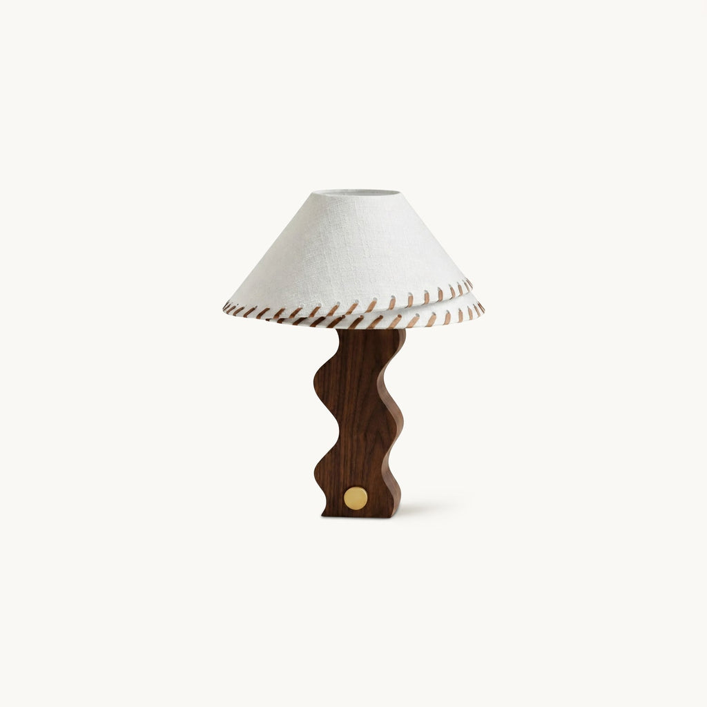 Walnut table lamp from Clérachic with a wavy sculpted base, a brass dial and a white linen shade stitched with leather lacing.
