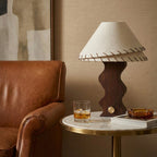 Table lamp from Clérachic on a round marble-topped side table beside a tan leather armchair, its shade lit softly.