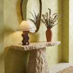 Small Clérachic table lamp on a rough stone console under an arched mirror, next to a vase of dried eucalyptus.