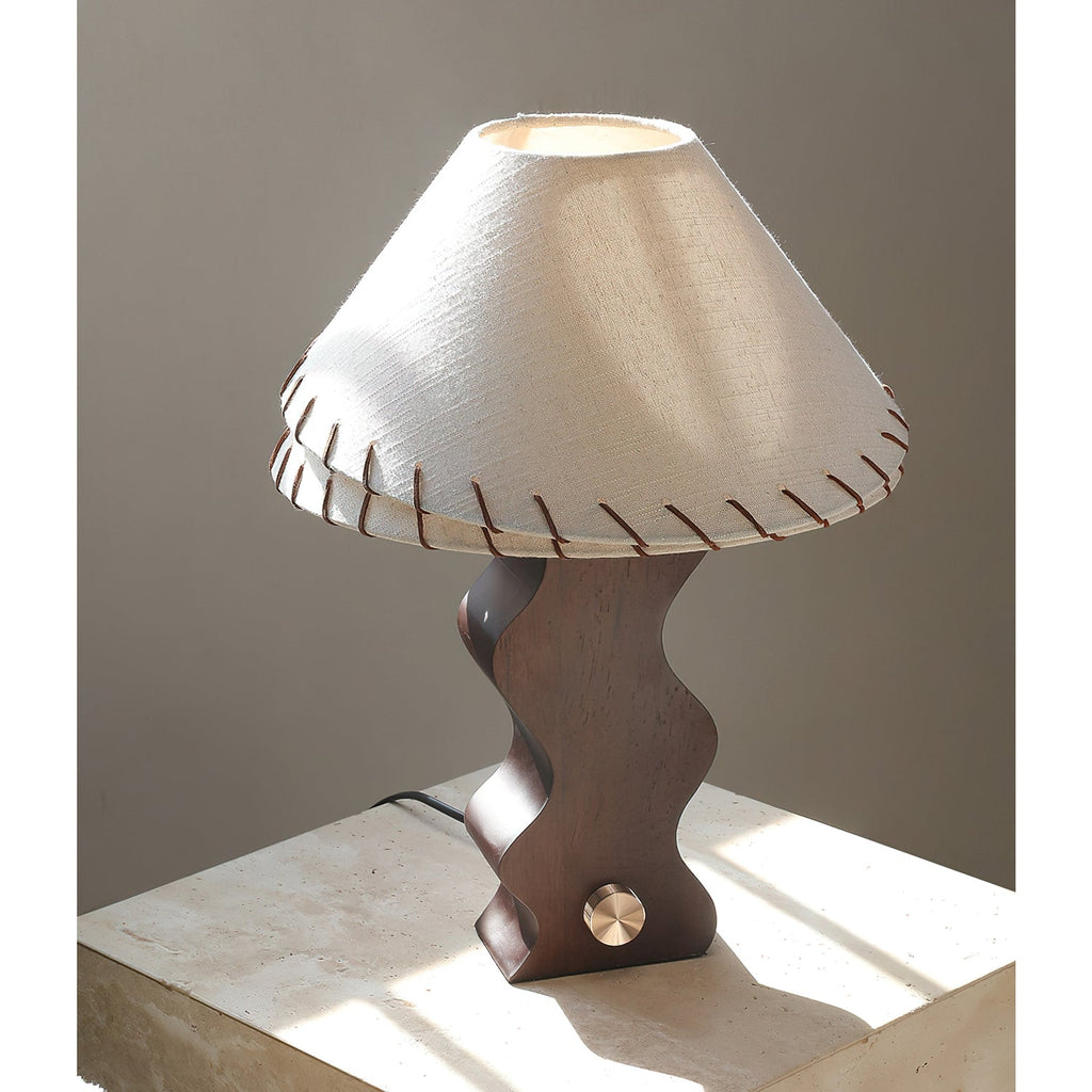 Walnut table lamp from Clérachic on a pale travertine block in sunlight, its brass dial catching the light.