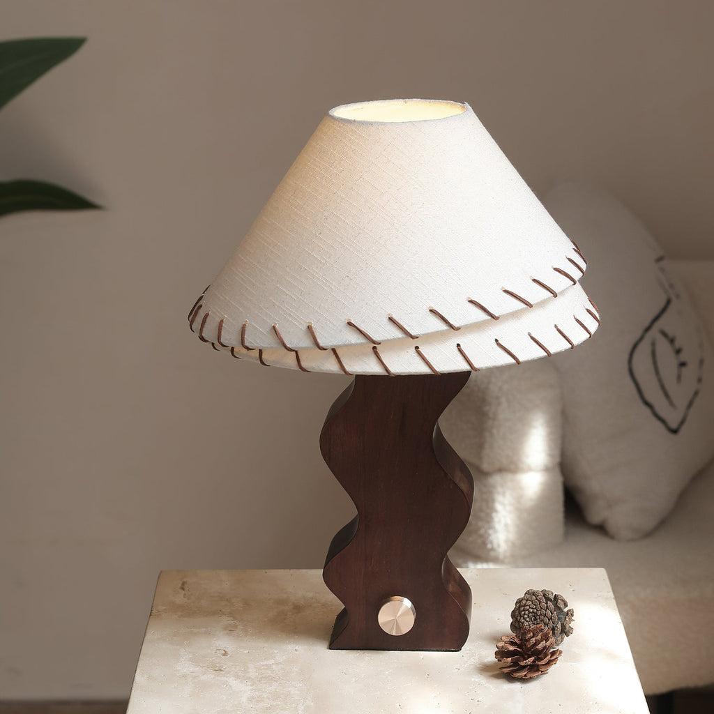 Wavy walnut-base Clérachic lamp on a travertine block, with a pine cone by its brass dial and a cushion behind.