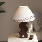 Wavy walnut-base Clérachic lamp on a travertine block, with a pine cone by its brass dial and a cushion behind.
