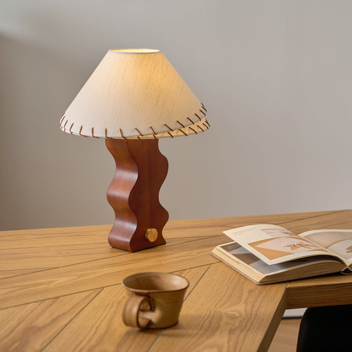 Table lamp from Clérachic on a herringbone oak desk, with an open book and a stoneware mug nearby.