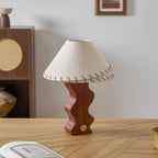 Unlit white linen shade on a Clérachic walnut lamp, set on an oak desk before a rattan-front cabinet and a vase.