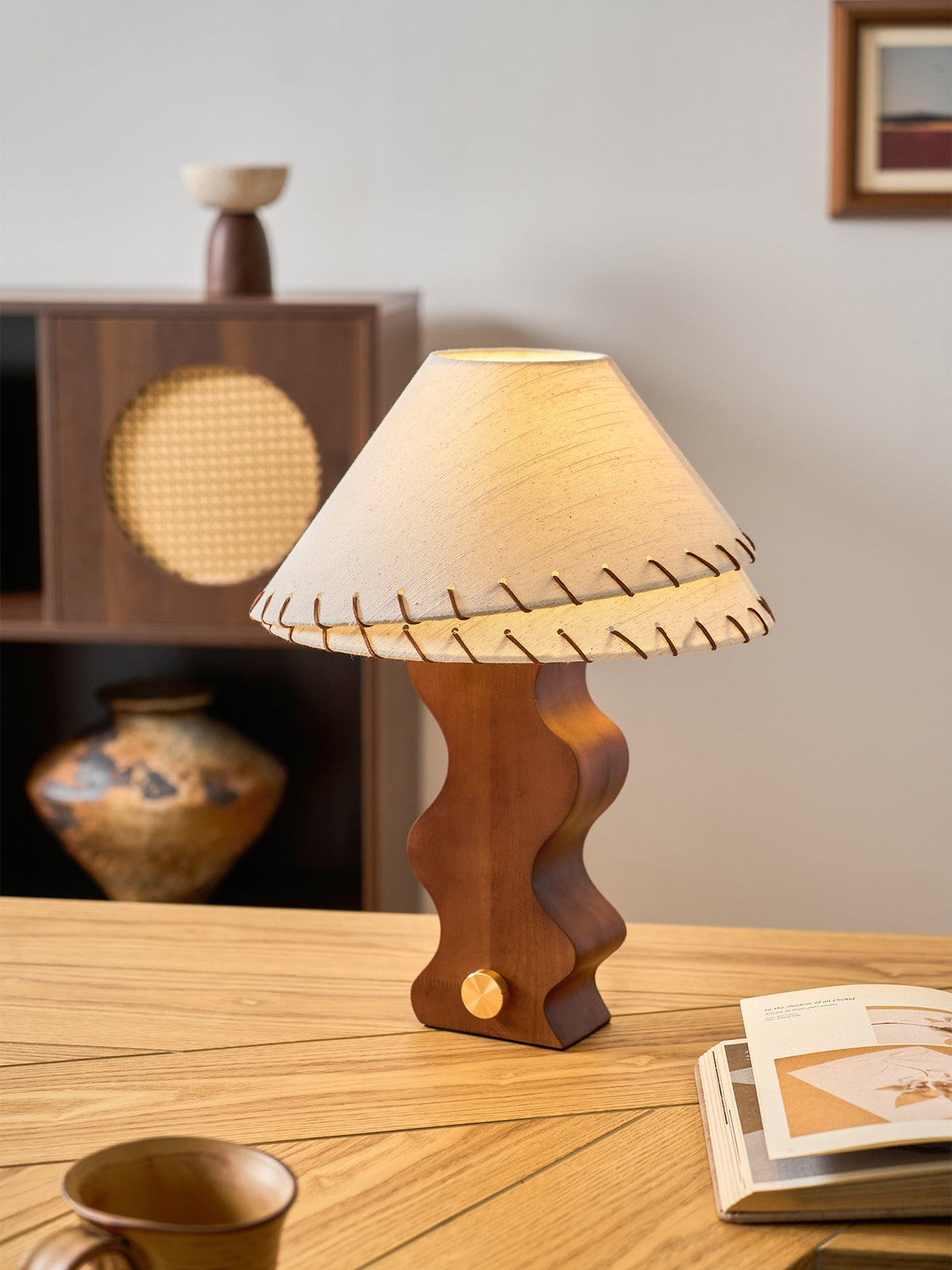 Clérachic table lamp on an oak desk, with an open book at the right and a rattan-door cabinet in the background.