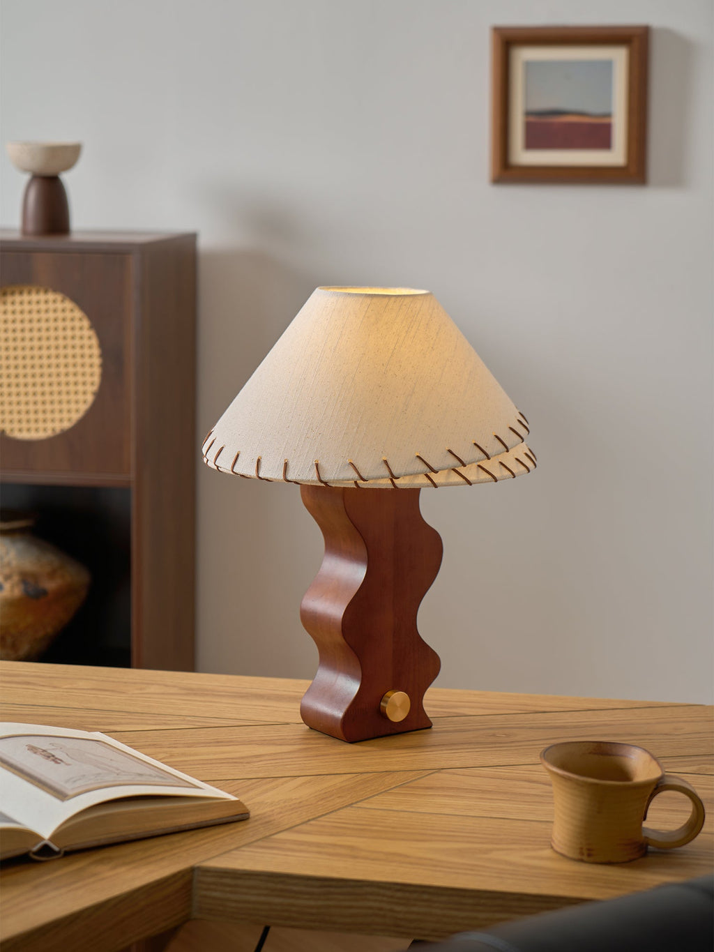 Walnut-base Clérachic lamp with its laced shade, on an oak desk with a mug at the right and a small framed print above.