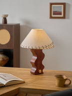 Walnut-base Clérachic lamp with its laced shade, on an oak desk with a mug at the right and a small framed print above.