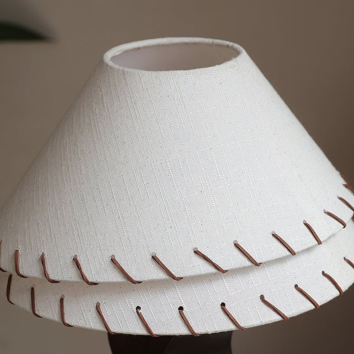Close view of the woven linen shade and brown leather stitching around the two tiers of this Clérachic table lamp.