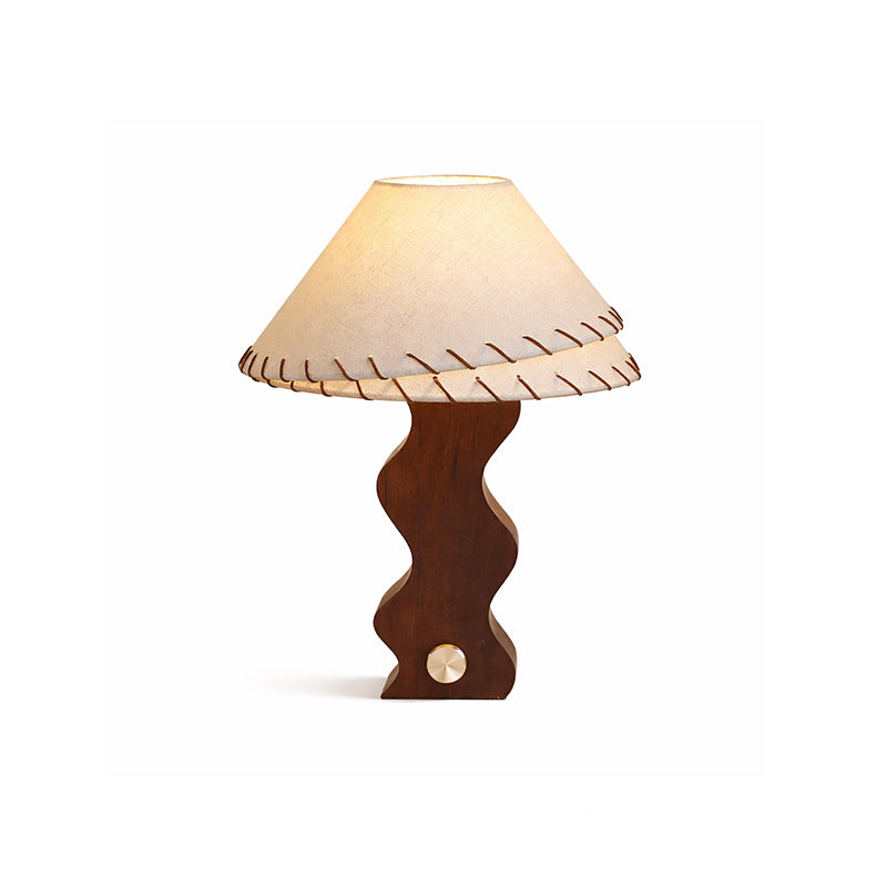 Lit Clérachic table lamp on a white backdrop, with a warm glow through the linen shade above the wavy walnut base.