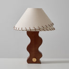 Clérachic table lamp on a light surface against grey, unlit, showing the laced shade and the wavy base with its brass dial.
