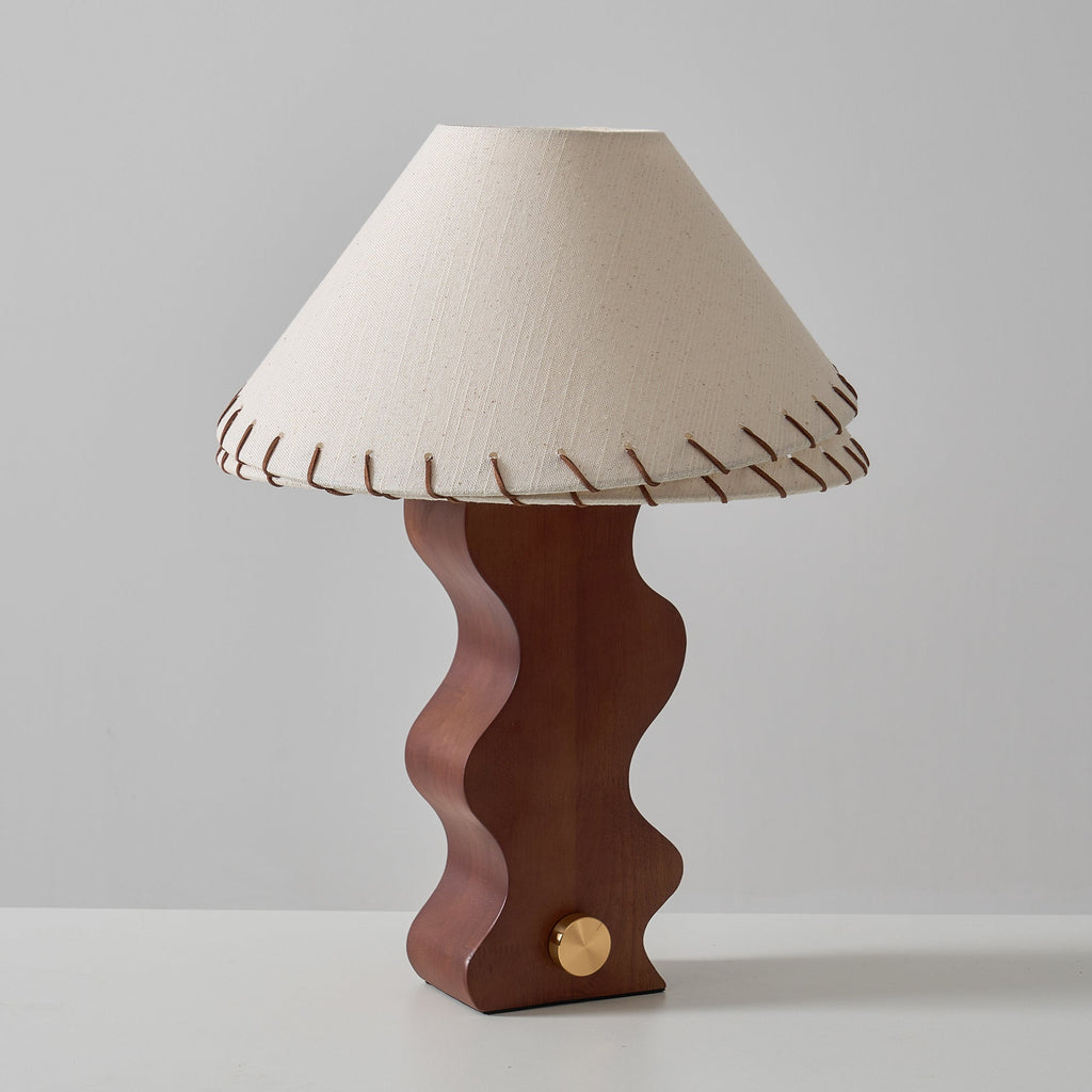 Front view of a Clérachic table lamp with a cream linen shade and a deep brown wavy base, photographed against grey.
