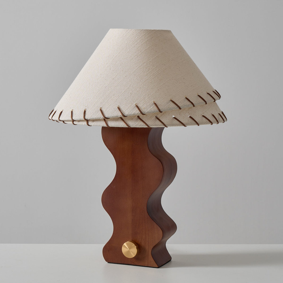 Straight-on view of the Clérachic walnut lamp with its two-tier stitched shade and brass dial, on a white tabletop.