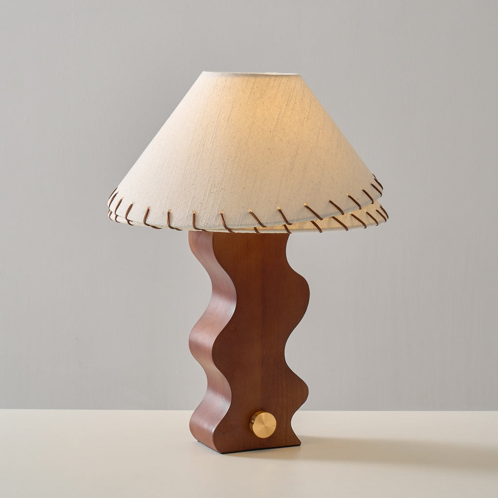 Lit Clérachic table lamp in a three-quarter view, with warm light inside the shade and a soft shadow on the grey wall.