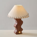Clérachic walnut table lamp switched on, the glow lighting the underside of its stitched linen shade, against grey.