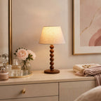 Lit Clérachic bead-column lamp on a cream dresser with pink roses, perfume bottles and a folded blanket beside it.