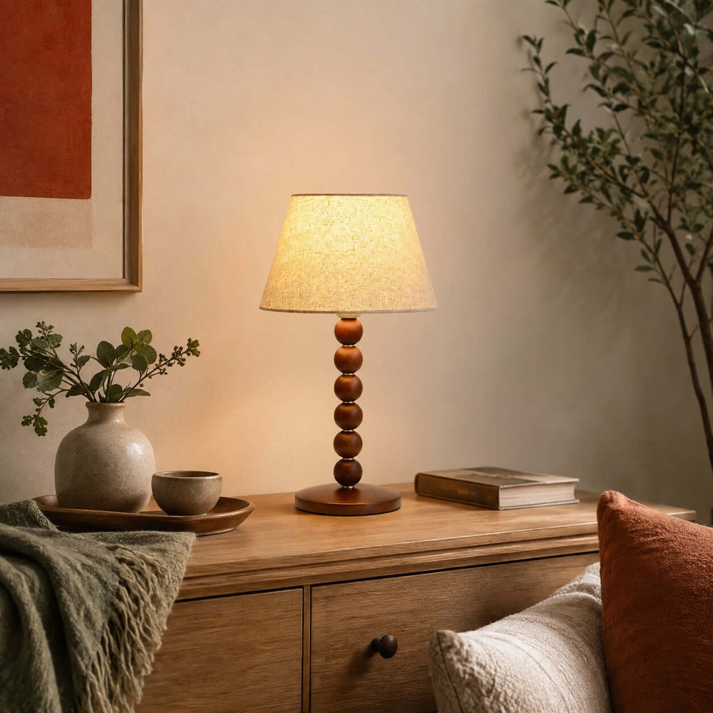 This Clérachic lamp glows on a wooden sideboard beside a ceramic vase, a small bowl and a stack of books.