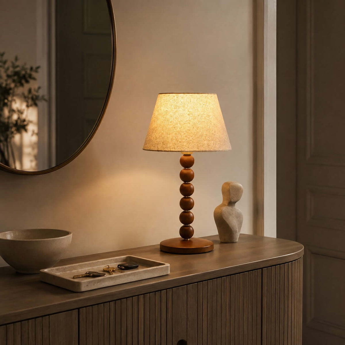 Warm light from this Clérachic lamp falls over a fluted wooden console, a pale bowl, a tray of keys and a round mirror.