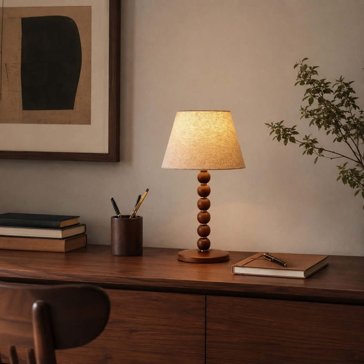 Clérachic stacked bead lamp on a dark wood desk, with a pen pot, a notebook and a framed print behind it.