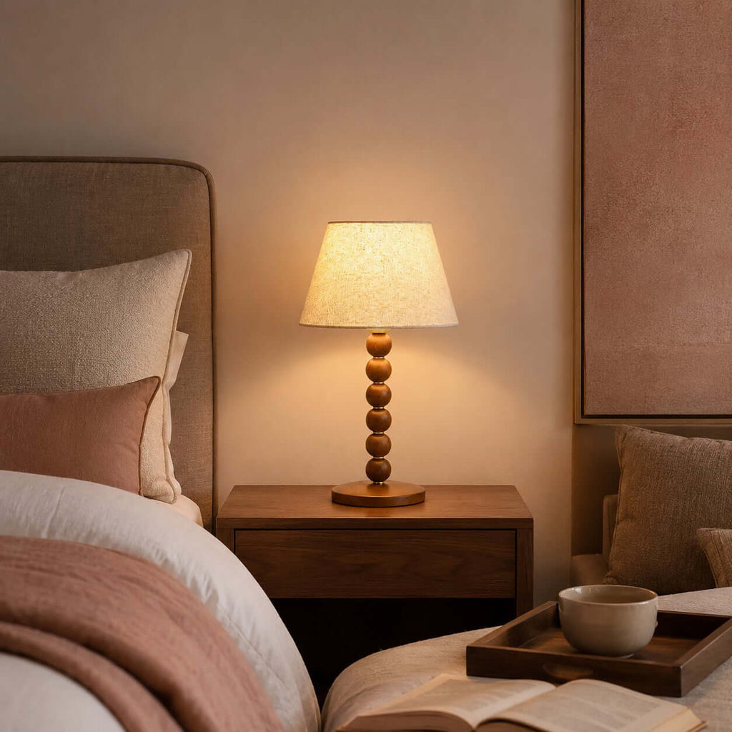 This Clérachic lamp lights a bedside table next to an upholstered headboard, with a tray, a cup and an open book on the bed.