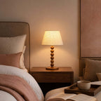This Clérachic lamp lights a bedside table next to an upholstered headboard, with a tray, a cup and an open book on the bed.