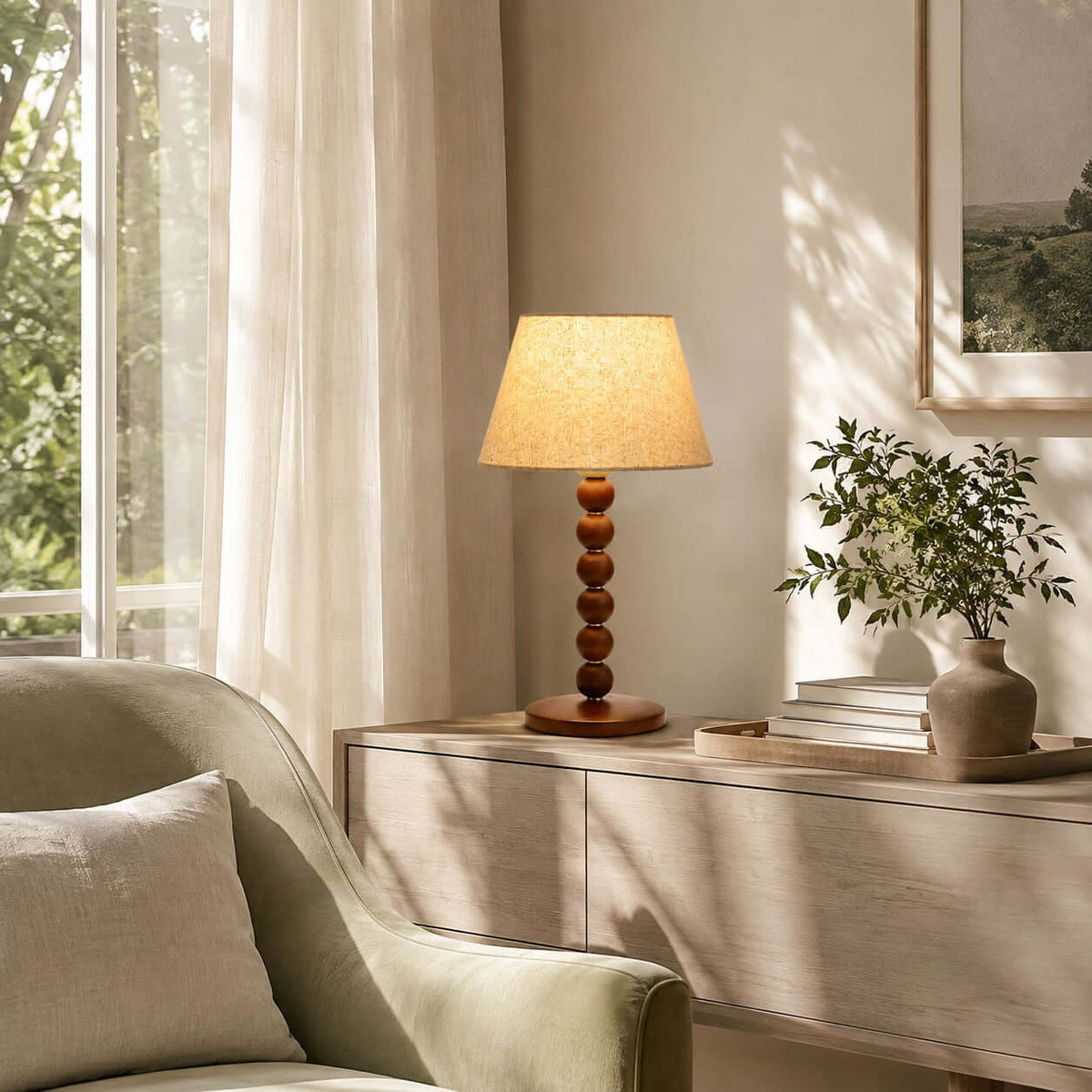 Daylight through sheer curtains falls near this Clérachic lamp on a pale console, with a potted plant and an armchair in sage green.