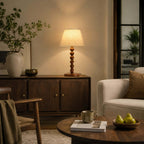 Beside a dark wooden sideboard and a round coffee table with pears, a Clérachic bead-base lamp gives off a soft golden glow.
