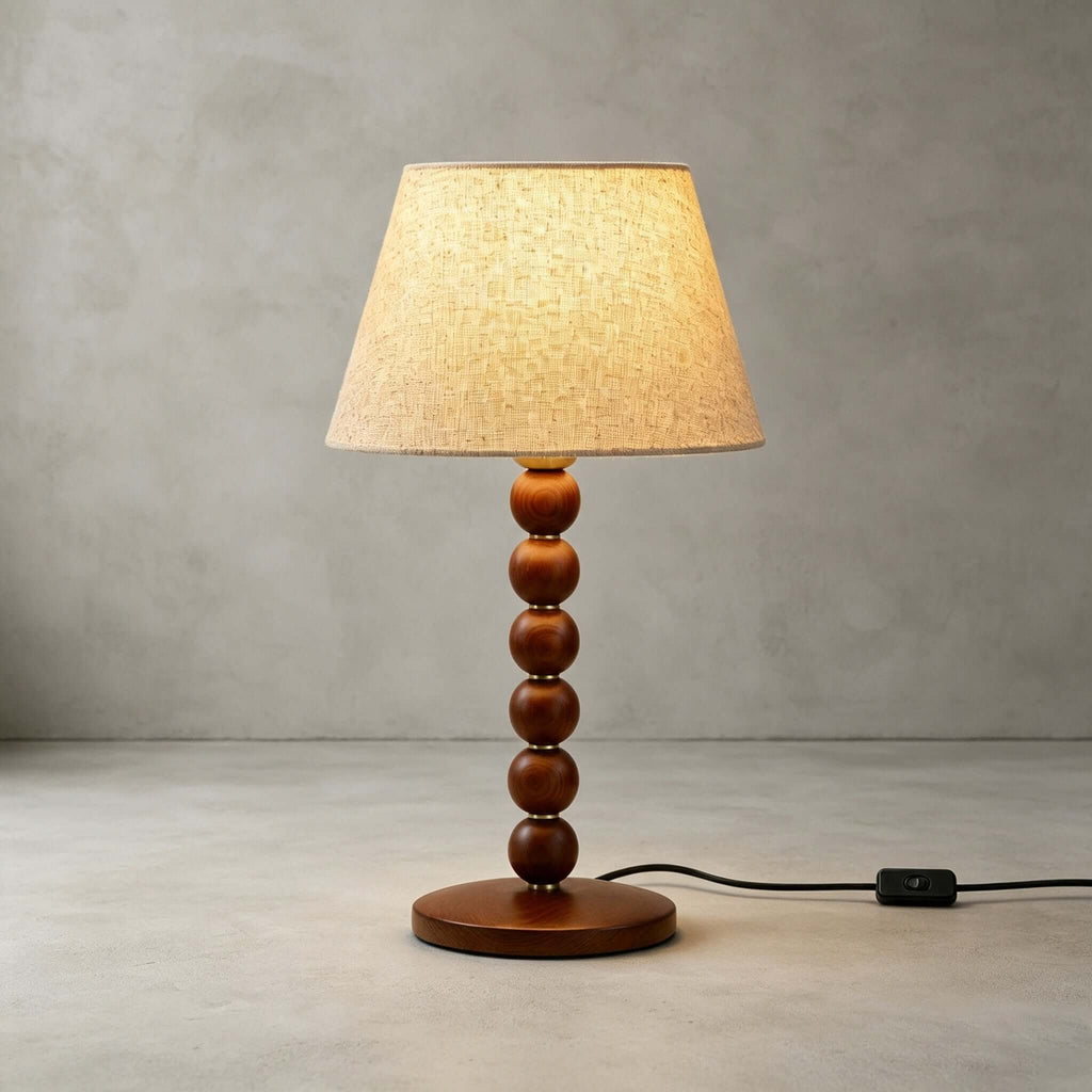 The walnut-finish beaded stem, round wooden base and beige fabric shade of this Clérachic lamp, on a plain concrete-grey floor.