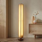 Slim Clérachic floor lamp lit warm in a calm room, beside a pale wood sideboard holding a vase with dried stems.