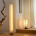 Clérachic floor lamp beside a driftwood branch, with a smaller matching table lamp lit on a low platform behind.