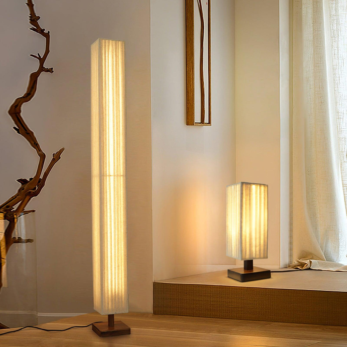 Clérachic floor lamp beside a driftwood branch, with a smaller matching table lamp lit on a low platform behind.