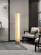 Clérachic floor lamp standing in a tall grey-and-white living room, beside a black-framed chair and a grey rug.