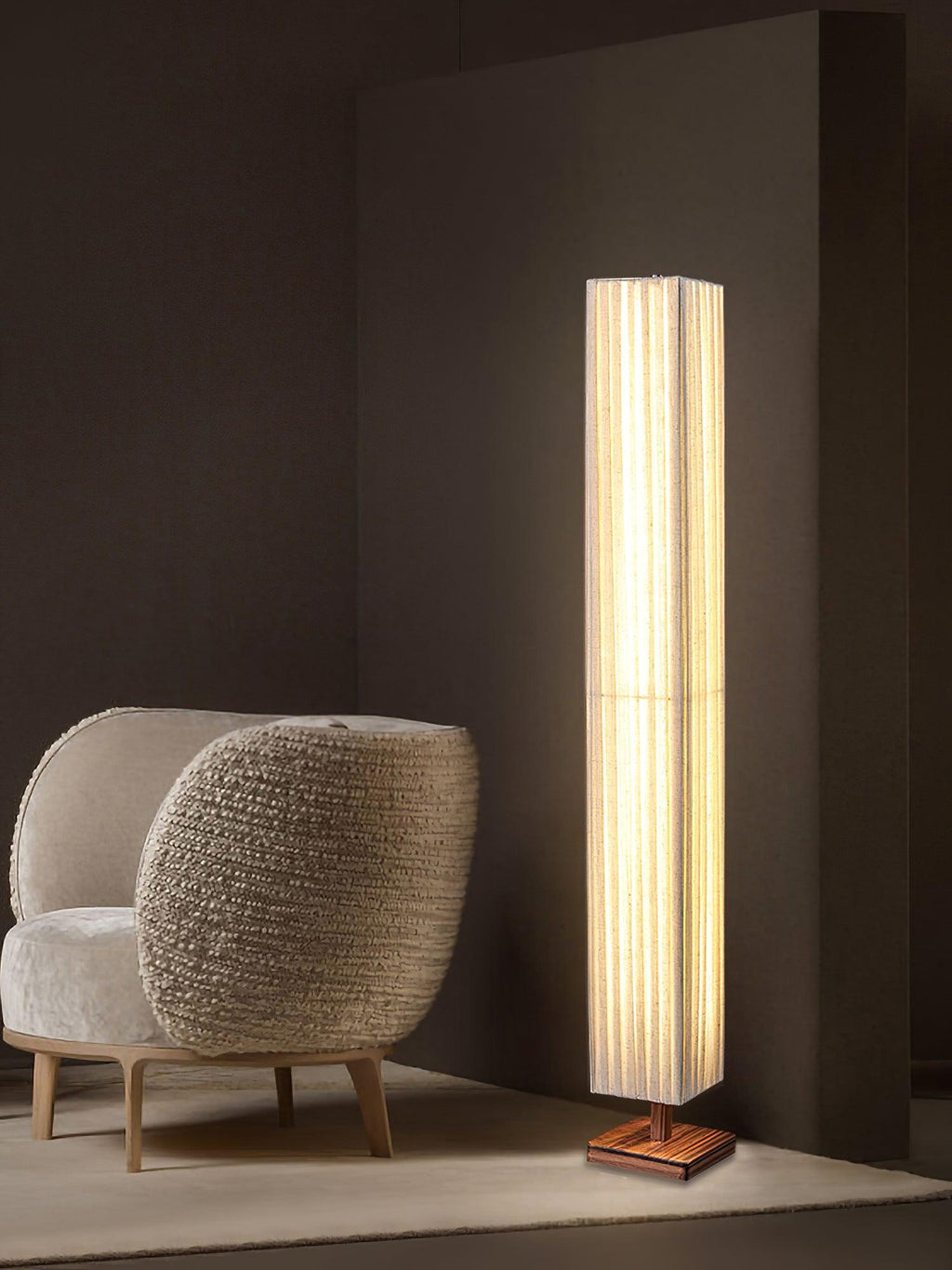 Beige pleated Clérachic floor lamp in a dark corner, with a bouclé armchair and a pale rug beside it.