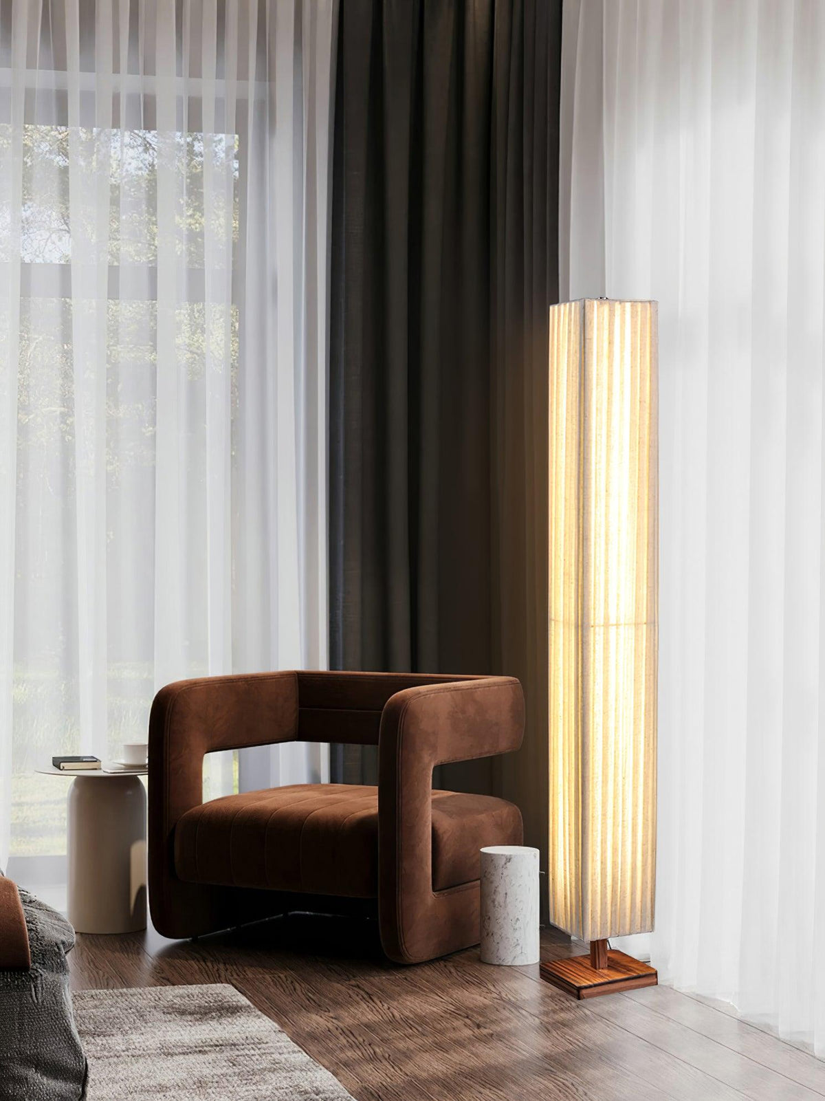 Lit Clérachic floor lamp beside a rust-brown armchair, with floor-length sheer and dark curtains behind.