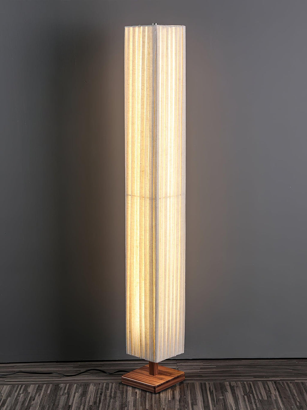 Lit Clérachic floor lamp on a square walnut base, with a cord trailing across a dark wood floor against a grey wall.