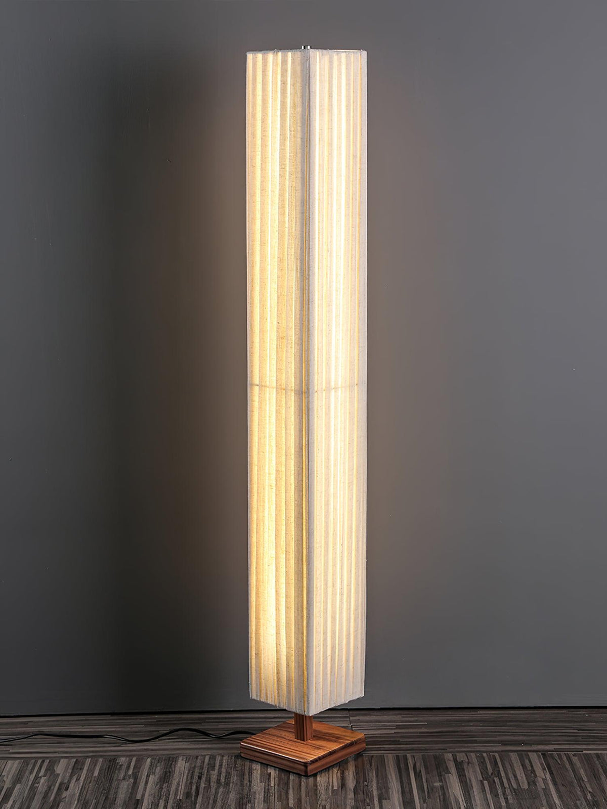 Lit Clérachic floor lamp on a square walnut base, with a cord trailing across a dark wood floor against a grey wall.
