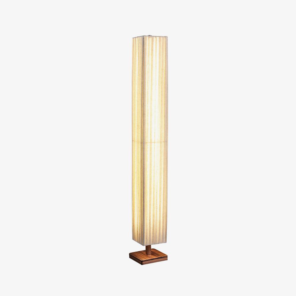 Tall pleated Clérachic floor lamp lit warm on a square wooden base, in a three-quarter view on a light grey backdrop.