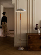 Clérachic floor lamp with a walnut stem and chrome shade stands in a hallway on parquet, beside a dark wood chest of drawers.