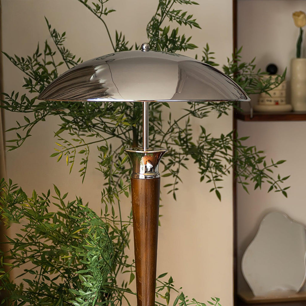 Chrome dome shade and walnut stem of this Clérachic floor lamp, set among leafy branches against a pale wall.