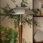 Chrome dome shade and walnut stem of this Clérachic floor lamp, set among leafy branches against a pale wall.