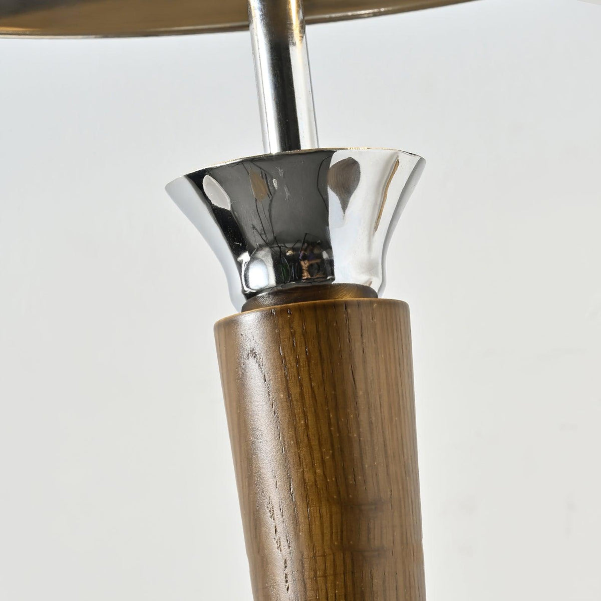 Close view of the walnut stem and flared chrome collar on this Clérachic floor lamp, against a plain pale backdrop.